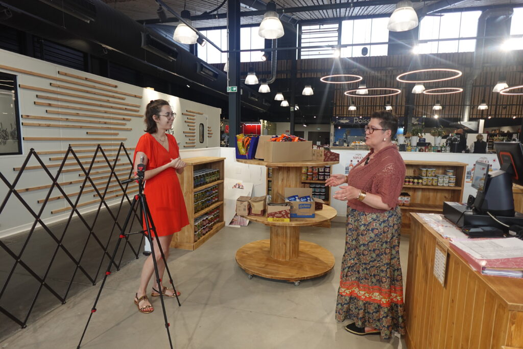 Marie-Charlotte Richard, fondatrice de l'agence T-Rex, en tournage terrain avec une commerçante aux Halles de Bernicourt pour la gestion de leur communication digitale